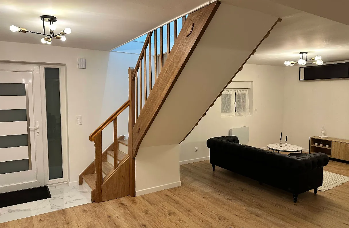 Pièce de vie rénovée, murs blancs et escalier en bois