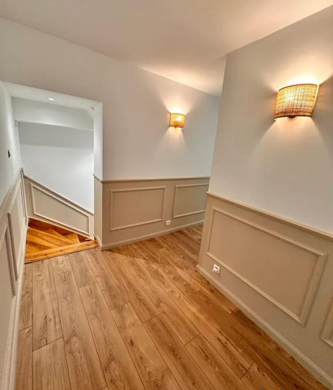 Couloir rénové : soubassements moulurés beige lin, murs blancs, appliques en rotin