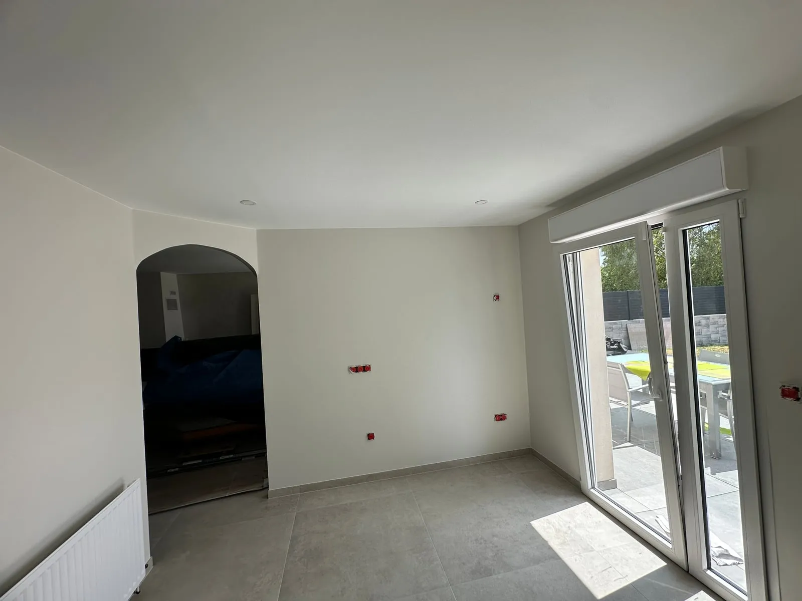Pièce rénovée aux murs et plafond blancs et lisses, avec une ouverture en arche et une baie vitrée